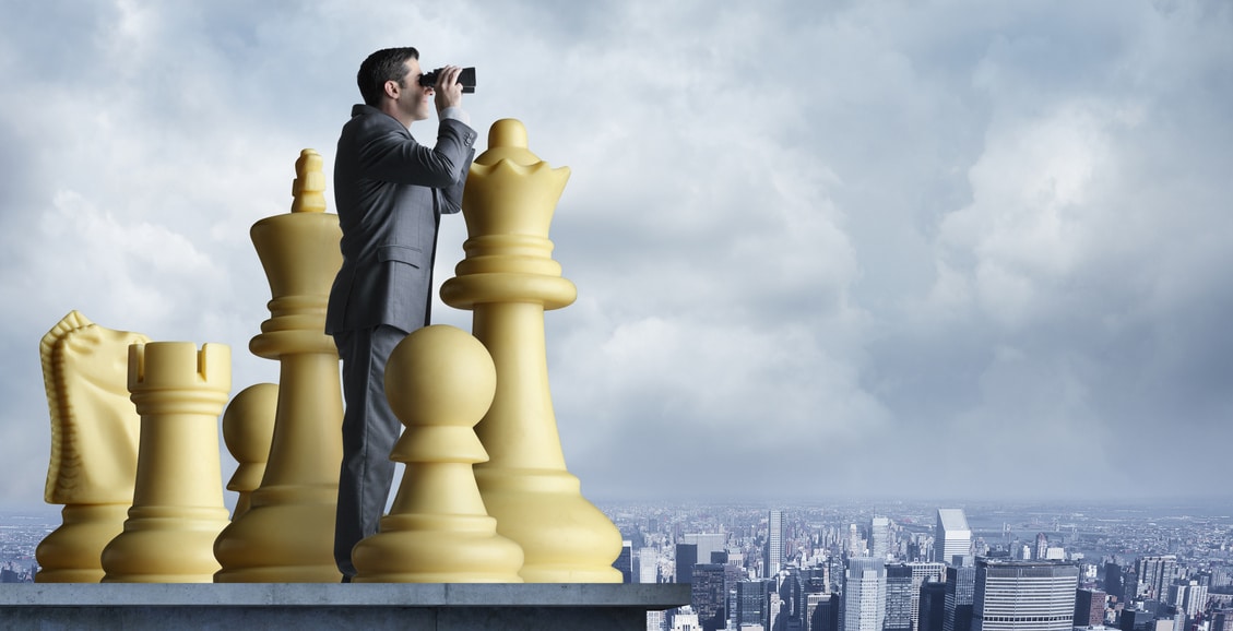 Businessman standing among chess pieces looks through binoculars